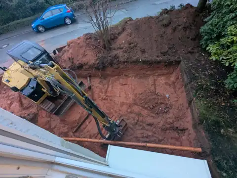 Minibagger in einer Baugrube neben einem Wohnhaus