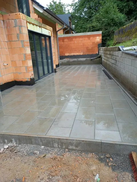 Große Terrasse aus hellgrauen Platten an einem Neubau, gebaut von C&H-Bau